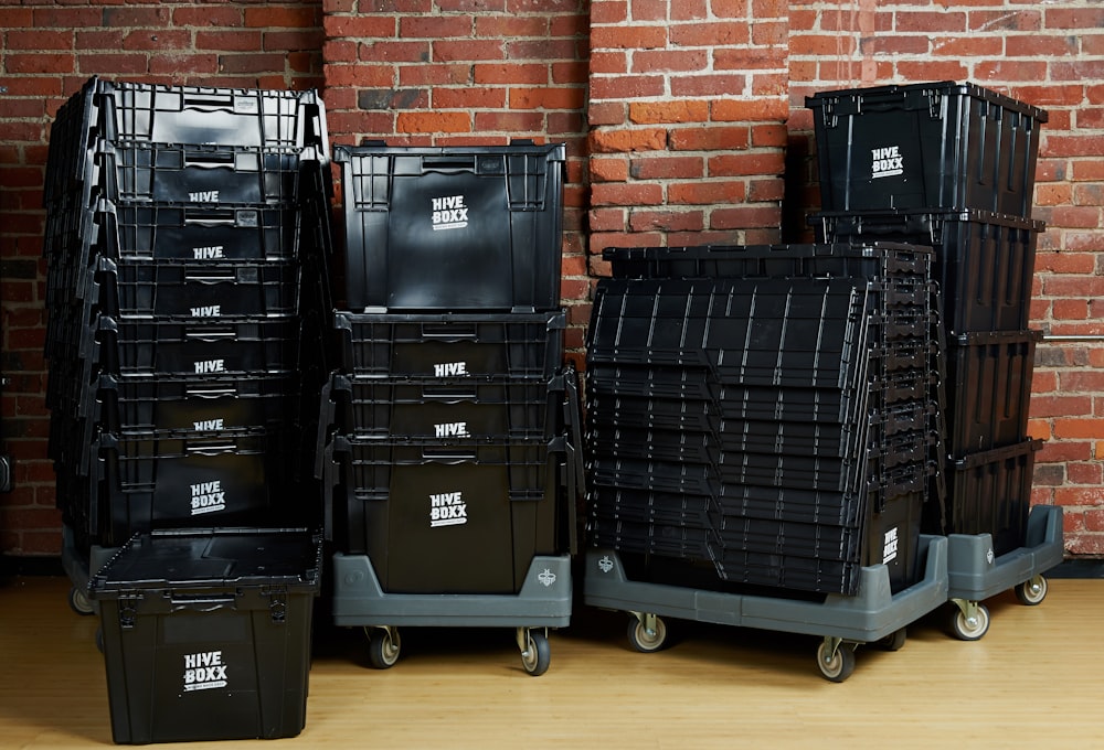 Stacked black latching storage totes against a brick wall